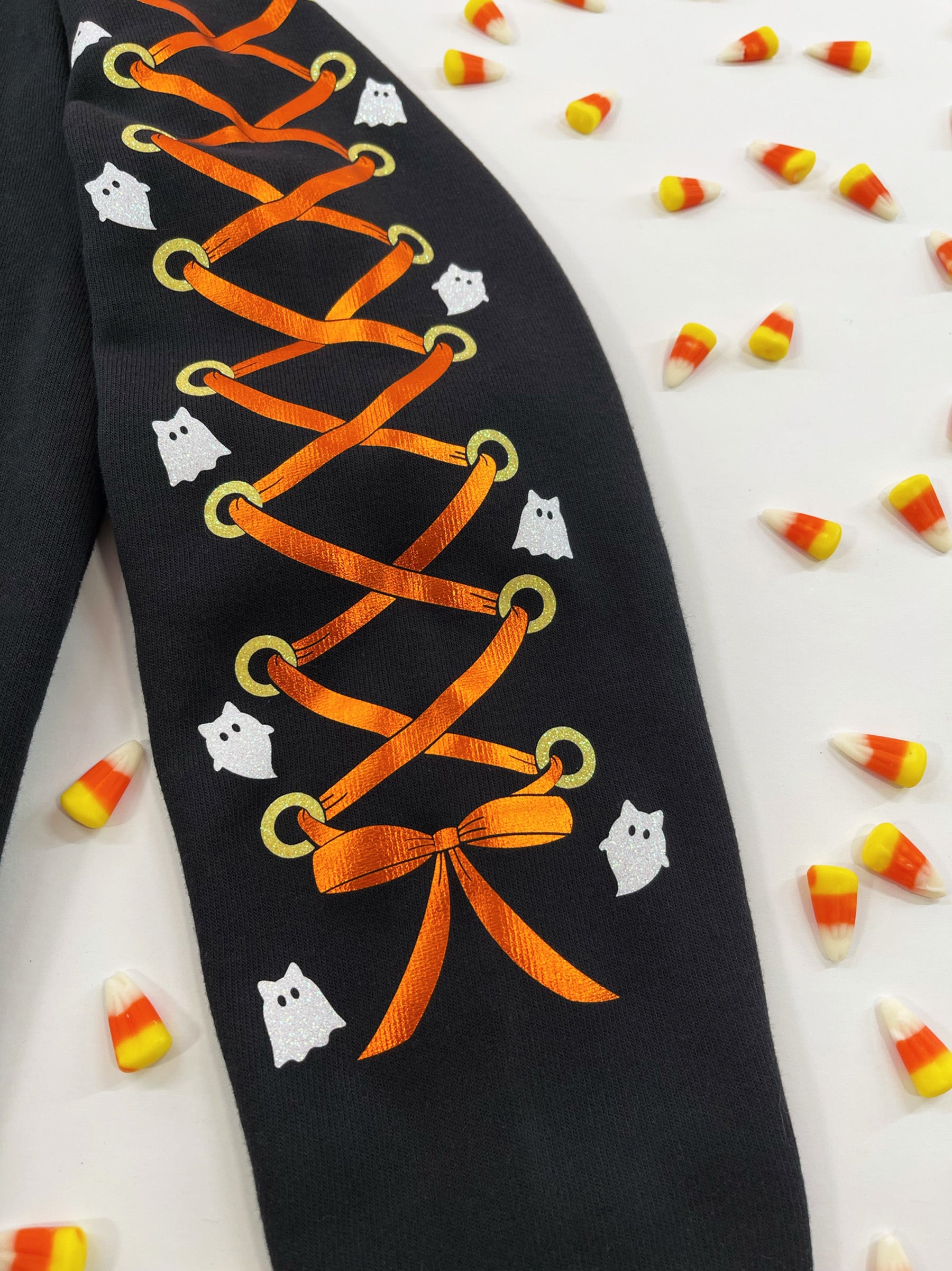 Close up of sleeve with orange metallic lace-up, glittery yellow grommets, white cat ghost designs.