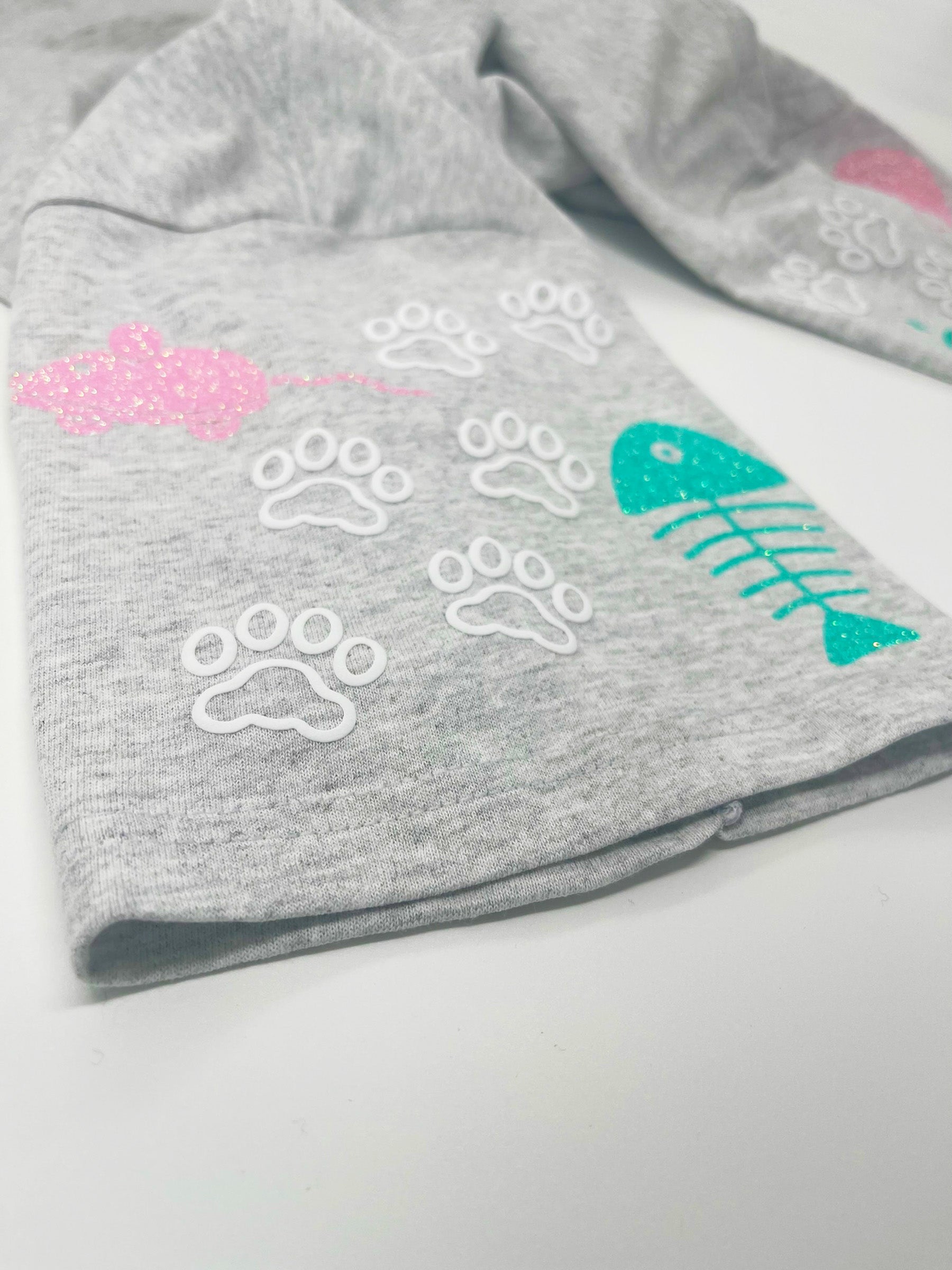Close up of right sleeve with toy mouse and fish bone glitter designs and white cat paws.